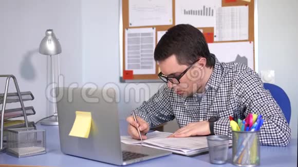 经理在工作场所填写纸质表格查看笔记本电脑显示器视频的预览图