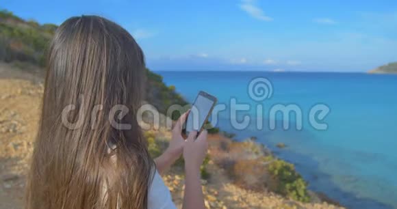 有魅力的女性用智能手机制作海洋照片山和清澈的碧水视频的预览图