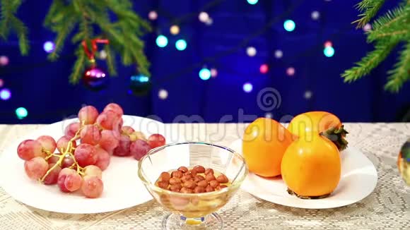 柿子葡萄和坚果加蜂蜜桌子上有一棵装饰好的圣诞树闪烁的动名词模糊了视频的预览图