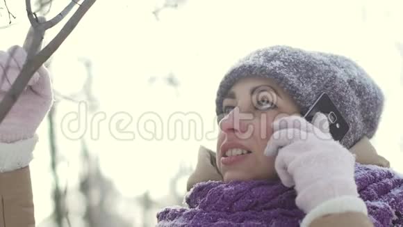 在白雪覆盖的冬林中散步时幸福的女人在电话中交谈的肖像视频的预览图