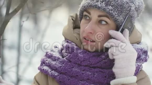 在白雪覆盖的冬林中散步时幸福的女人在电话中交谈的肖像视频的预览图