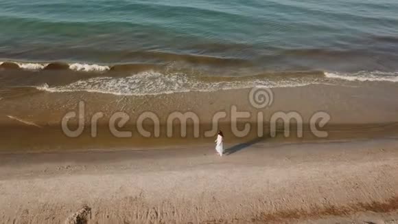 穿着白色裙子的女孩沿着海滩散步视频的预览图