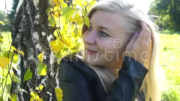 公园里快乐美丽的金发女人微笑着抚摸头发秋天的背景慢动作视频的预览图