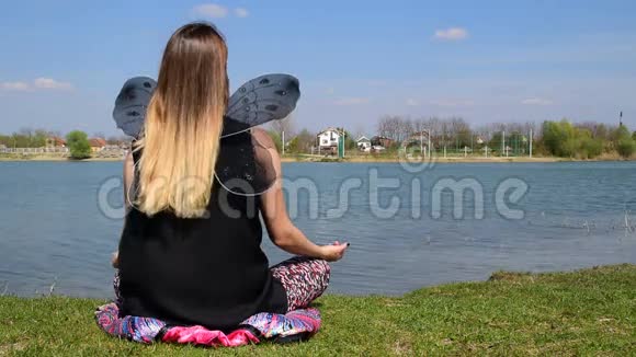 有蝴蝶翅膀的女孩坐在平静的水旁边的莲花位置上沉思视频的预览图