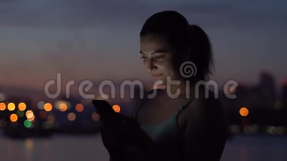 一个女孩在夜城的背景下使用智能手机慢动作视频的预览图