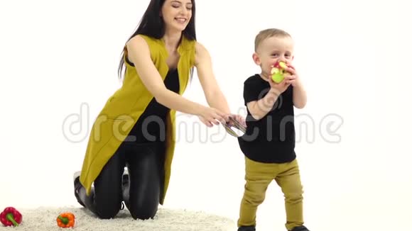 女孩坐在地板上旁边的蔬菜躺着她试图抱着孩子白色背景慢动作视频的预览图