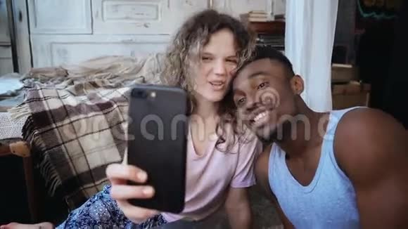 美丽的多民族夫妇在智能手机上拍摄自拍照片女人拿着智能手机男人吻她笑视频的预览图