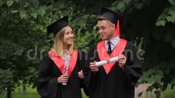 微笑着两个毕业生在公园里散步拿着文凭说话视频的预览图