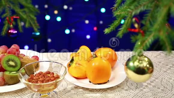 猕猴桃葡萄和坚果加蜂蜜桌子上放着一个装饰好的圣诞树球灯光模糊视频的预览图