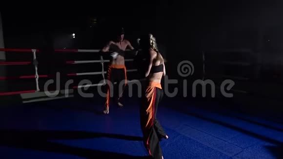 一个戴着头盔和拳击手套的女孩在黑暗中在拳击场上打的家伙剪影慢动作视频的预览图