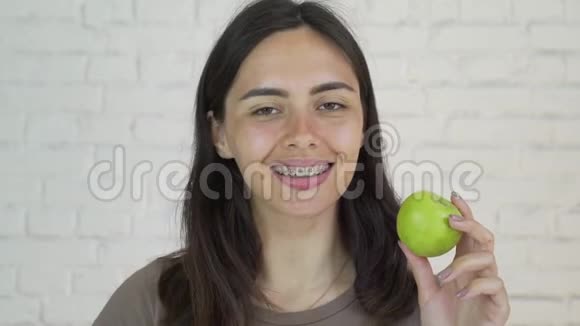 戴着牙套的女人吃着绿苹果微笑着白色的特写视频的预览图