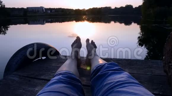 双脚躺在靠近湖塘的码头上视频的预览图