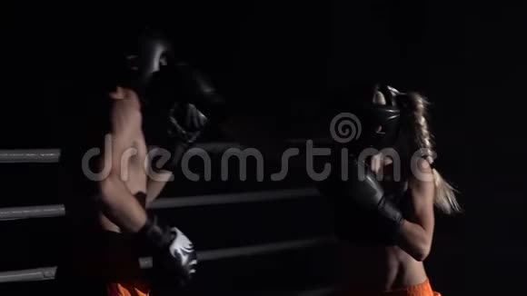 戴着头盔戴着拳击手套的女孩在黑暗中在擂台上打慢动作视频的预览图