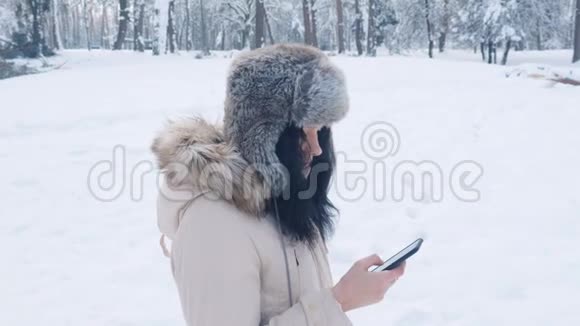 年轻的白种人戴着温暖的帽子在冬天下雪的时候使用智能手机视频的预览图