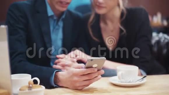 一对年轻夫妇在手机屏幕上滚动浏览照片讨论他们在现代城市咖啡馆的一个中热闹地约会视频的预览图