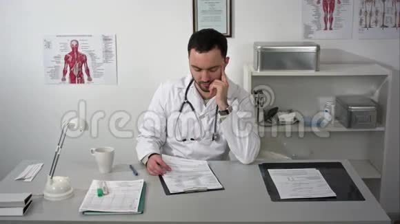 年轻的严肃医生坐在医疗办公室有文件夹和阅读文件视频的预览图