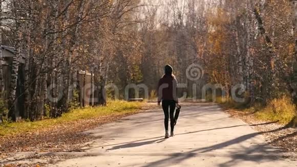 美丽的年轻女士在黄金时刻扛着三脚架在Autmn的森林路上走来走去视频的预览图