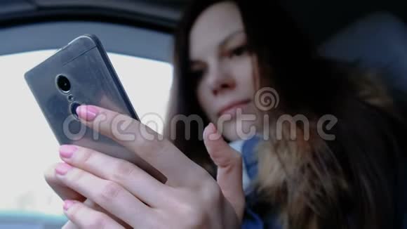 有手机的女人在车里年轻漂亮的黑发女人在手机里看东西视频的预览图