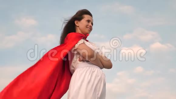 超级英雄女孩穿着红色斗篷站在田野上斗篷在风中飘扬特写镜头女孩梦想成为一个视频的预览图