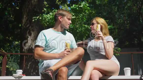 快乐的一对夫妇吃热狗在城市公园的长凳上玩得很开心4K慢动作视频的预览图