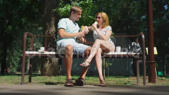 快乐的一对夫妇吃热狗在城市公园的长凳上玩得很开心4K慢动作视频的预览图