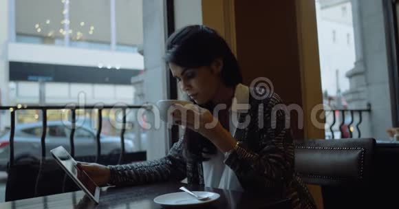 年轻女子坐在城市的咖啡馆里用平板电脑看电影4k视频的预览图