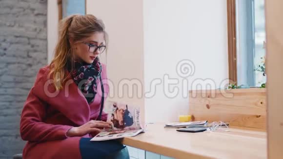 舒适的咖啡馆一个的内部迷人的欧洲女孩穿着时尚的休闲服坐在窗边翻页视频的预览图