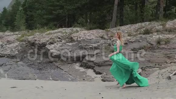 年轻的女人穿着一件长长的流动的衣服在河山的背景上穿着绿色衣服的女人视频的预览图