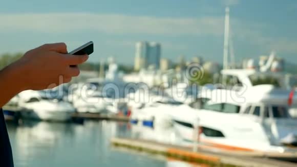 男性手握智能手机在带有游艇的港口模糊背景下视频的预览图