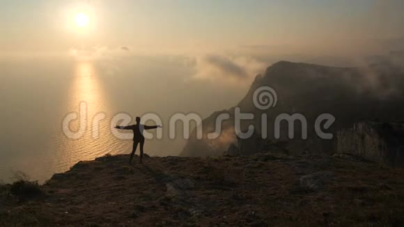 西尔休特年轻女子张开双臂从克里米亚的一座高山上观察海上美丽而壮观的日落视频的预览图