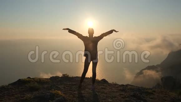 西尔休特年轻女子张开双臂从克里米亚的一座高山上观察海上美丽而壮观的日落视频的预览图