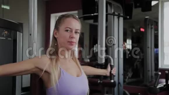 一个身材漂亮的运动女性在健身房的模拟器上训练胸肌视频的预览图