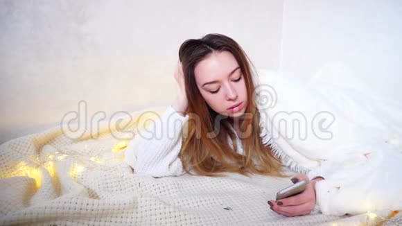迷人的女孩为取消会议而感到悲伤并在智能手机屏幕上阅读信息躺在被覆盖的地板上视频的预览图