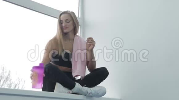 美丽的女孩在明亮的健身房锻炼美丽的女孩坐在窗户上用手机自拍视频的预览图