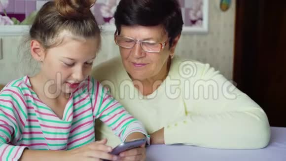 年轻可爱的孙女教祖母如何在家里使用智能手机视频的预览图