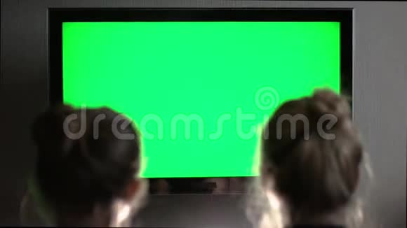 两个年轻的长发金发金发在晚上的家庭内部看绿色屏幕电视视频的预览图
