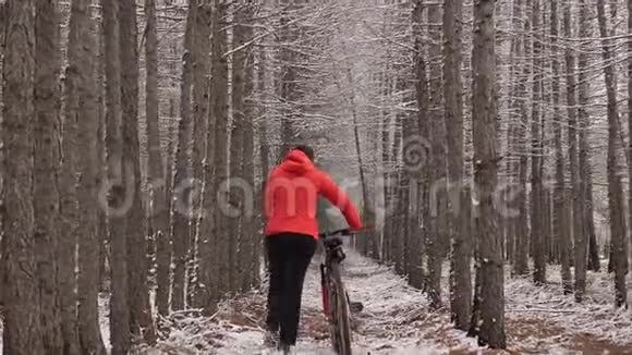 那个女人骑着自行车走在树林里的一条小路上穿橙色夹克的女人和狗一起散步骑自行车的运动女孩视频的预览图