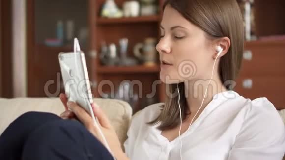 开朗的年轻女性带着耳机听音乐唱歌敲智能手机屏幕视频的预览图