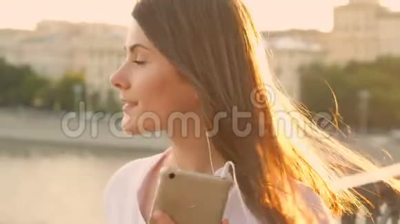 快乐的年轻女人在户外放松漂亮的女孩在她的智能手机上听音乐夏日阳光灿烂视频的预览图