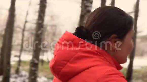 那个女人骑自行车在树林里的小路上走穿橙色夹克的女人和狗一起散步冬天的森林视频的预览图