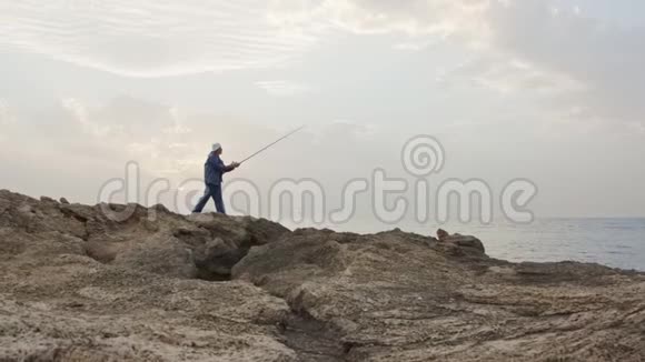 老渔夫站在海边的岩石上在夕阳下钓鱼视频的预览图