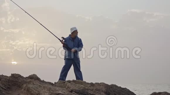 老渔夫站在海边的岩石上在夕阳下钓鱼视频的预览图