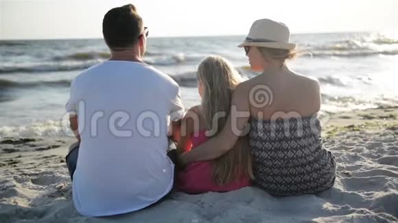 快乐的一家人坐在海滩上拥抱和看着海浪在暑假视频的预览图