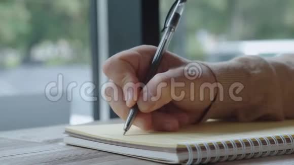 穿浅色毛衣的人用黑色钢笔在笔记本上写字特写视频的预览图
