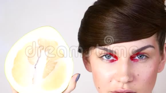 白色背景上的年轻女人的肖像一个女孩拿着半个柚子视频的预览图