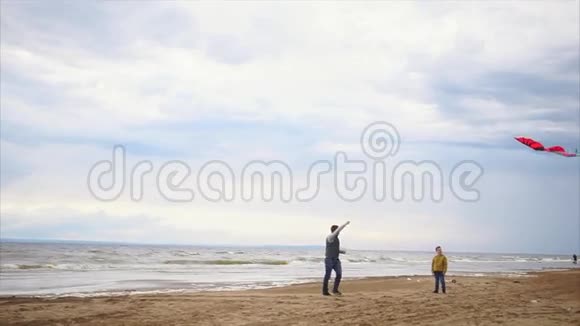 家庭乐趣带着儿子玩风筝的人他们沿着海岸奔跑视频的预览图