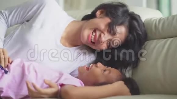 快乐的女孩和她的母亲在沙发上开玩笑视频的预览图