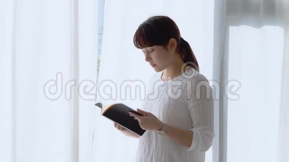 美丽的肖像年轻的亚洲妇女放松和休闲站在卧室的阅读书考试在家里视频的预览图