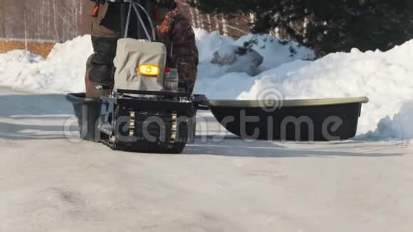 一辆小型雪车在一条有拖车和两名乘客的冬季道路上行驶视频的预览图