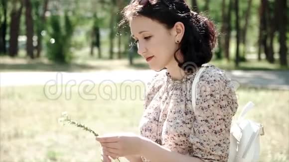 年轻女孩坐在草地上拿着一朵花看着镜头的肖像视频的预览图